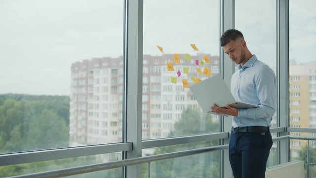 Office work with laptop and stickers. Young haired man holds a laptop in her hand and takes a sticker from the window and examines it. Businessman in the office at work.