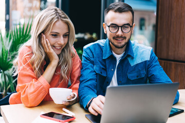 Positive caucasian male and female watching video on laptop computer co operating on project,20s...
