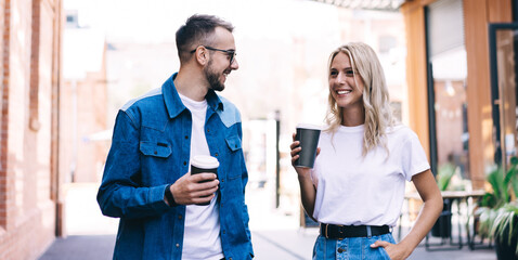 Funny caucasian male and female hipster friends talking to each other and joking on date walking on street, smiling woman and man colleagues satisfied with friendly conversation on free time