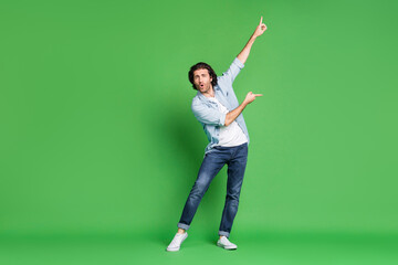 Fototapeta na wymiar Full length photo of young stubbled man raise arms indicate fingers dance wear denim shirt jeans sneakers isolated green color background