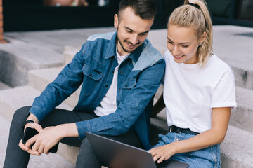 Fototapeta premium Positive caucasian male and female friends checking news and updates in social networks communicating, smiling hipster guys watching video together satisfied with 4G internet connection on laptop