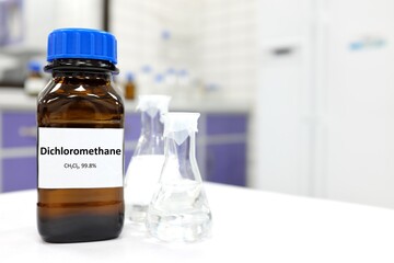 Selective focus of dichloromethane liquid chemical compound in dark glass bottle inside a chemistry laboratory with copy space. 