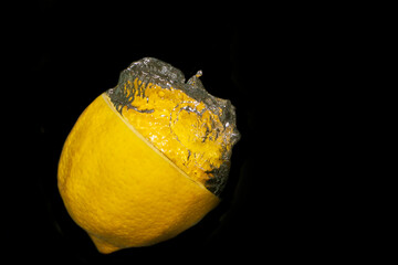 Yellow lemon thrown into water. There are bubbles of water above the lemon. The background is black.