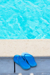 Blue summer flop-flops near edge of swimming pool.
