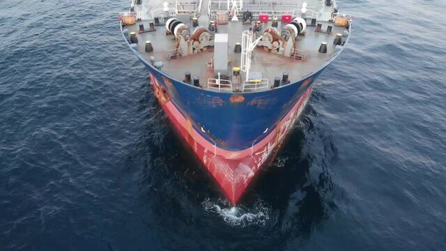 Aerial footage of the bow of a merchant ship at anchor and swaying on the waves.