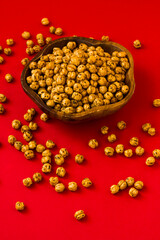 Double roasted yellow chickpeas in wooden bowl on red surface
