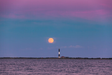 Full moon rising through a hazy horizon behind a beautiful lighthouse. Fire Island, New York.