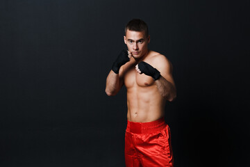 Sportsman muay thai man boxer stance in red truncks at black background