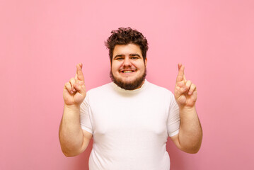 Positive young overweight man standing on a pink background looking into the camera, smiling with...