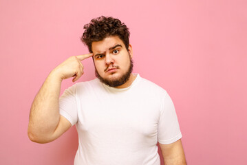 Obraz premium Serious bearded overweight man in a white T-shirt looks into the camera and shows a 