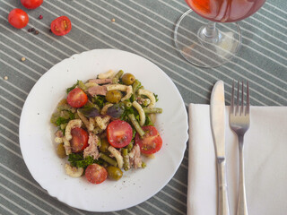 Pasta and tomato salad on a white plate with a glass of wine