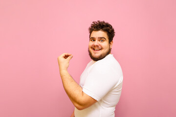 Portrait of a joyful fat guy on a pink background, emotionally happy to win and looking into the...
