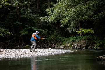 A fly fisherman fishing a trouts in mountain river