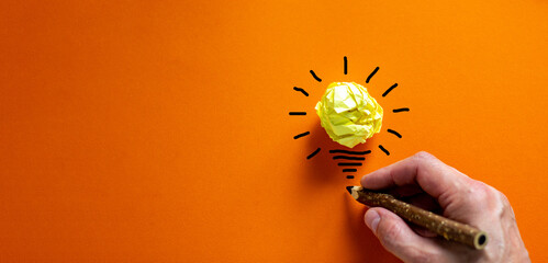 Idea and innovation concept image. Male hand with black pencil. Beautiful orange background.