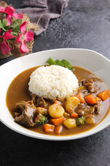 Japanese cuisine. Curry rice in a white deep plate on a black table. Restaurant menu. Background image, copy space