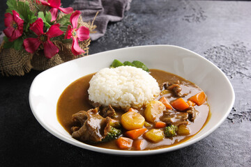 Japanese cuisine. Curry rice in a white deep plate on a black table. Restaurant menu. Background image, copy space