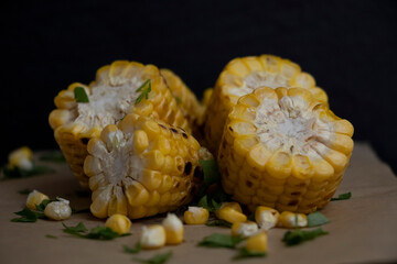 Fried corn on parchment paper with fine herbs and butter. Black background. Yummy.