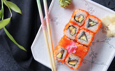 Japanese cuisine. Rice rolls with red caviar and wasabi on a white plate on a black table with chopsticks. Restaurant menu. Background image, copy space, flatlay