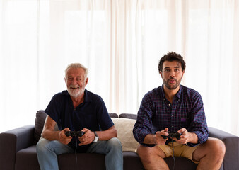 Happy senior father and adult son playing video game together at home. Elderly father and adult son...