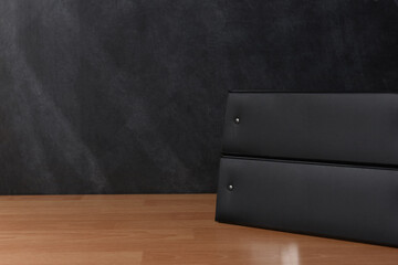 Two black binders on a teachers desk in front of a chalkboard.