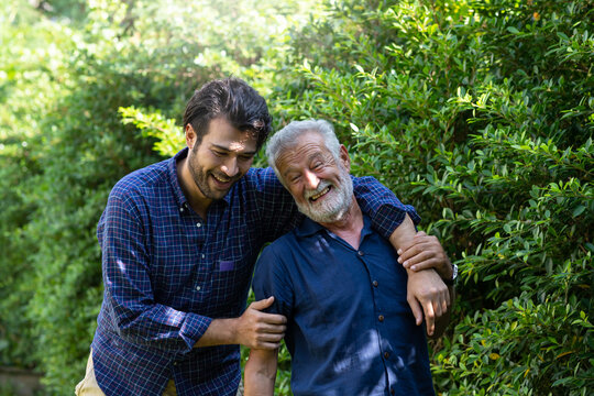 Smiling senior father with adult son embracing and talking outdoor garden. Elderly father and adult son spending time together. Happy family, holiday and people concept