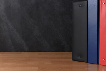 Three different binders standing on a teachers desk in front of a chalkboard.