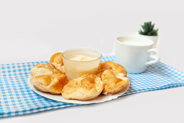 Small round eclairs or profiteroles lie on a blank background. Next to a plate with dessert on the table is a crumb of milk. Copy space