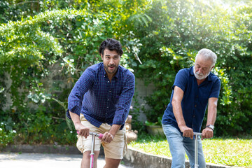 Naklejka na ściany i meble Happy senior father with adult son playing scooter together outdoor garden. Elderly father and adult son having fun on holiday in the backyard. people, family, holiday concept