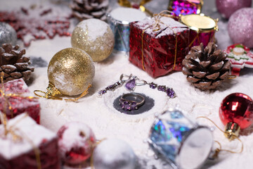 purple jewelry - ring and earrings - next to New Year's decorations in the snow. Christmas trees, balls, snowflakes, gifts, cones. Christmas mood. Flatly photo.
