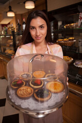 Vertical shot of a cheerful female confectioner smiling, holding tray of delicious tartelettes