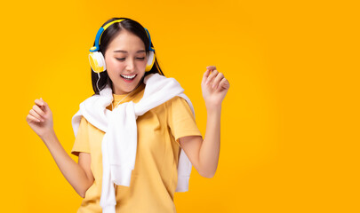 Gorgeous asian woman hanging sweater on shoulder and listening music in headphones and singing on yellow background. Charming girl dancing. Attractive lady enjoying favorite song. copy space