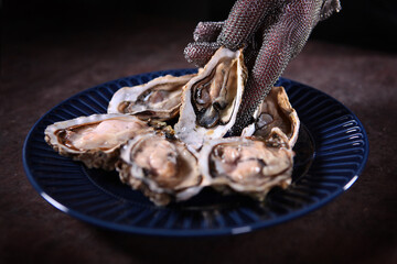 Blue plate with open fresh oysters. A gloved hand puts an oyster on a plate. Unrecognizable photo.