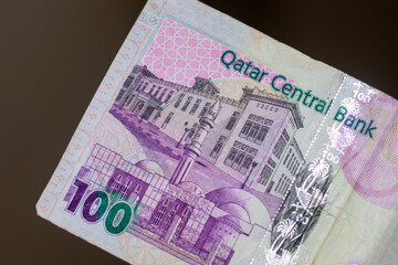 Currency of the Qatar - purple one hundred rial or riyal notes spread out on a brown background. Money exchange.