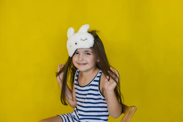 A little girl on a bright yellow background wearing a fashion accessory sleep mask.