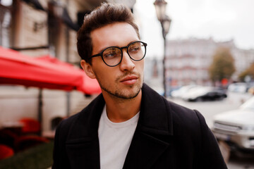 Obraz premium Confident young man in full suit looking away while standing outdoors in european city. Wearing eyewear. Stylish hairstylr. ..