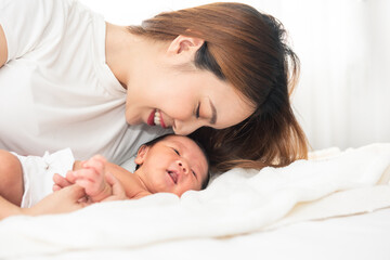 Fototapeta na wymiar Beautiful asian women mother long hair in the white pajamas. mom kiss at newborn infant with love, while a baby sleeping in her arm with warm, safe, comforted resting on the clean bed.