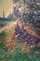 child in beautiful dress lying in colorful autumnal leaves