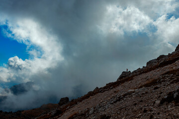 Silhouette of a man standing on a rock in the mountains of the Italian Dolomites. There are dramatic clouds with blue skies in the sky.
