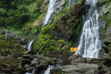 A beautiful waterfall with people standing facing the waterfall looking happily.