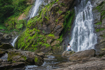 Woman sitting on a rock with a waterfall in front.