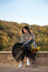 Naklejka na ściany i meble Girl sitting on nature background in blanket of autumn leaves in her hands. Vertical frame