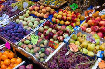Fruit stand at a market. Boxes with handwritten prices of 
peaches, berries, pears, figs, plums, grapes, pineapples and more. Focus on the peaches in the middle