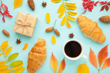 Fototapeta na wymiar Autumn or winter composition. Cup of coffee, gift, dried autumn leaves, croissant on blue background. Flat lay, top view, copy space