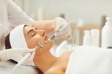 Woman receiving apparatus facial microcurrent treatment from therapist in beauty salon