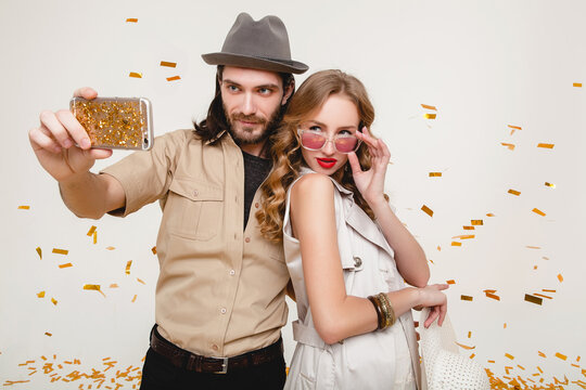 young stylish hipster couple in love making self photo, celebrating disco party, having fun, amazed, exited, funny face, golden confetti, holding phone, trendy apparel, cruise style, white background