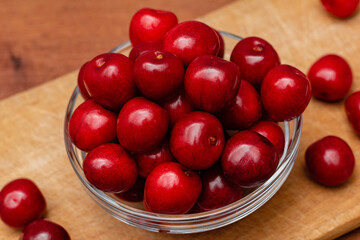 red fresh cherries in glass plate on wooden board on a wooden background
