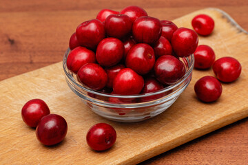 red fresh cherries in glass plate on wooden board on a wooden background