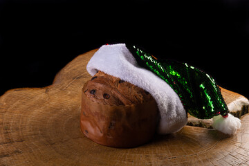 Panettone with chocolate chips and Santa Claus hat on rustic wood with black background, selective...