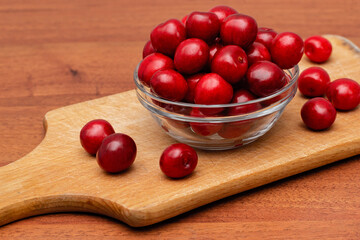fresh black cherries in glass plate on wooden board on a wooden background