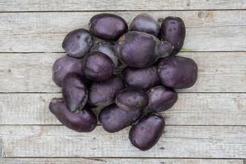 Raw harvested indigo potato tubers on a background of wooden boards.